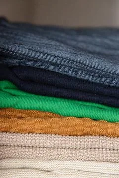Stack of folded knit sweaters in different colors neatly arranged on a shelf Stock Photos