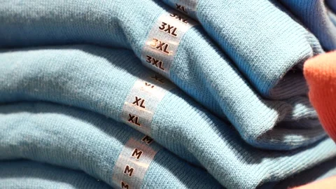 Stack of folded light blue cotton shirts showing size stickers in retail st.. Stock Footage 332578228
