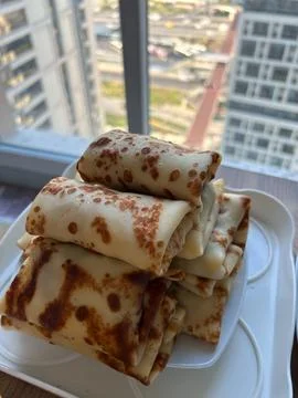 Stack of folded pancakes on a white plate near a window in a high-rise Stock Photos