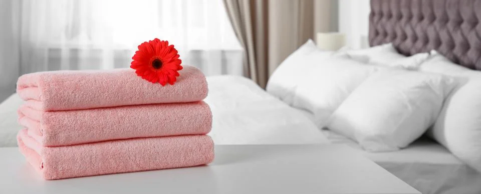 Stack of folded pink towels with red gerbera on bed indoors, space for text.  스톡 사진