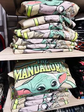 Stack of folded t-shirts featuring The Mandalorian character and title desi.. Foto stock