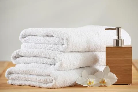Stack of folded towels, orchid flowers and dispenser on wooden table 写真素材