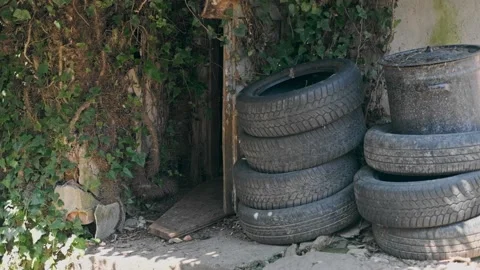 Stack of footage: Old tires piled up by an abandoned building, 4k Stockbeeldmateriaal 163594702