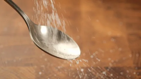 Stack of footage: White sugar fall through teaspoon down on a brown wood Stockbeeldmateriaal 128215325