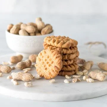 A stack of fresh homemade peanut butter cookies surrounded by peanuts. Stock Photos