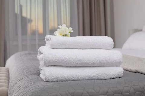 Stack of fresh towels with flowers on bed in hotel room 스톡 사진