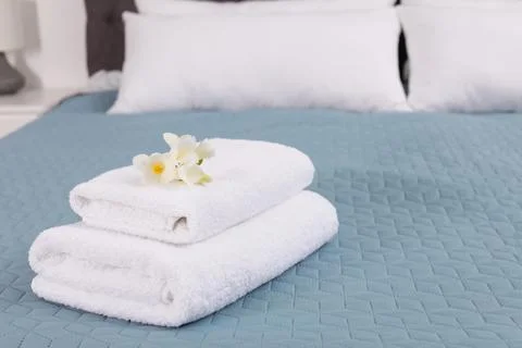 Stack of fresh towels with flowers on bed in hotel room 스톡 사진