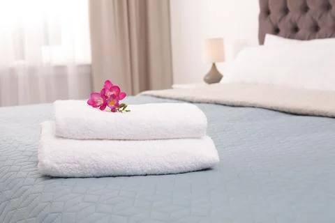 Stack of fresh towels with flowers on bed in hotel room 스톡 사진