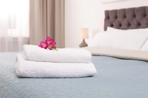 Stack of fresh towels with flowers on bed in hotel room Stockfoto's