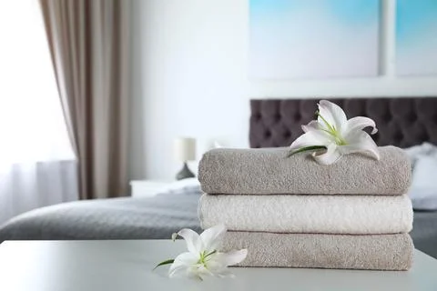 Stack of fresh towels with flowers on table in bedroom. Space for text 写真素材