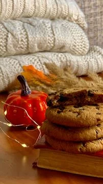 A stack of freshly baked cookies sits on a wooden surface beside a small orange Stock Photos