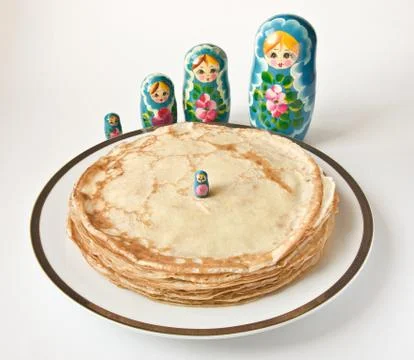 A stack of freshly made pancakes on a white plate and matryoshka dolls Stock Photos