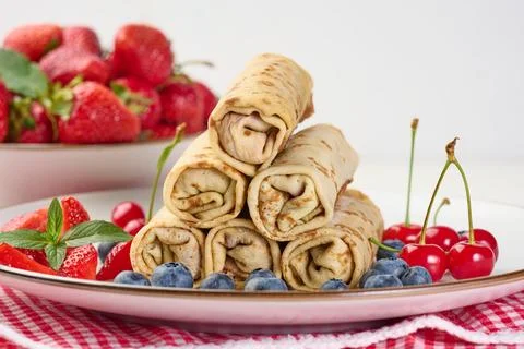 Stack of fried crepes with filling on a round plate, white table Stock-Fotos