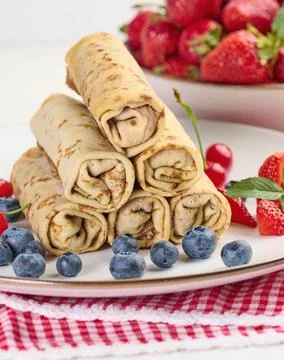 Stack of fried crepes with filling on a round plate, white table Foto stock