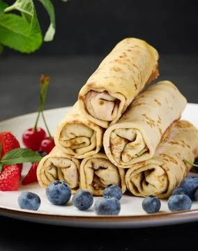 Stack of fried crepes with filling on a round plate, black table Stack of ... Stock-Fotos