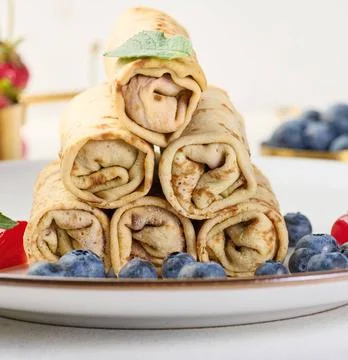 Stack of fried crepes with filling on a round plate, white table Stack of ... Stock-Fotos