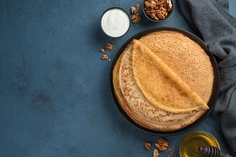 A stack of fried pancakes on a dark background with butter, honey and sour cr Stock Photos