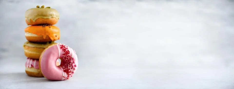 Stack of glazed colorful assorted donuts with sprinkles on grey cement Stock Photos