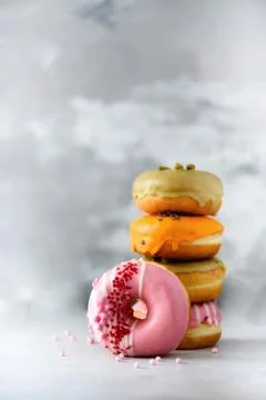 Stack of glazed colorful assorted donuts with sprinkles on grey cement Stock Photos