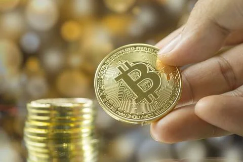 Stack of gold bitcoin coins in hand with golden bokeh background. Stock Photos