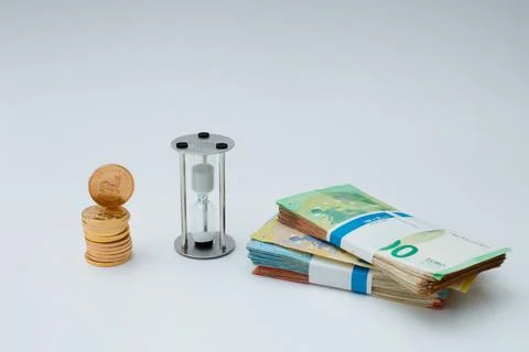 A stack of gold coins stands next to an hourglass Stock Photos