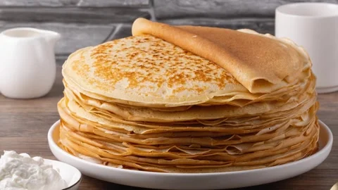 Stack of golden crepes served with sour cream on a wooden table Stock Footage 323007417