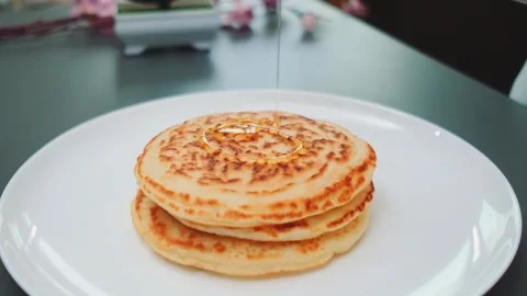 Stack of golden pancakes drizzling maple syrup indoors on white plate Stock Footage 342875592