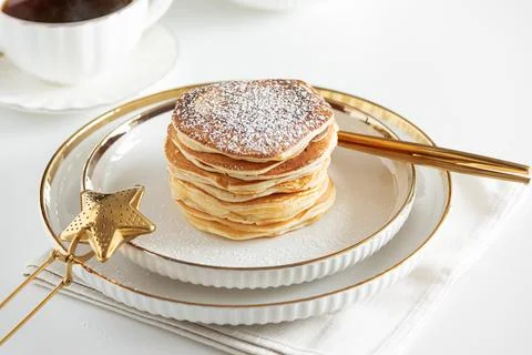 Stack of Golden Pancakes Dusted with Powdered Sugar with Coffee on White Tabl Stock Photos
