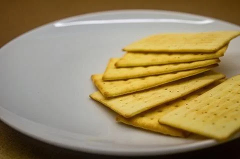The stack of golden, rectangular crackers on a white plate, with a soft foc.. Stock-Fotos