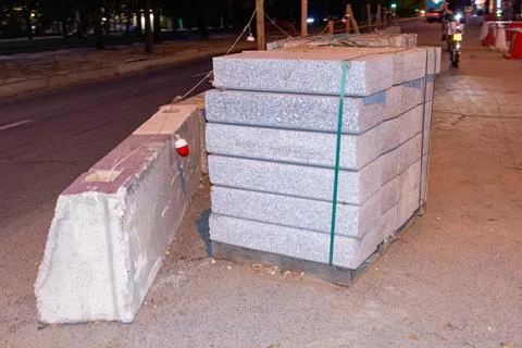 Stack of granite paving stones and concrete barrier on city street at night Stock Photos