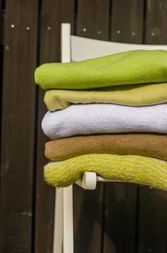 Stack of green and beige sweaters on white chair on wood background Stock Photos