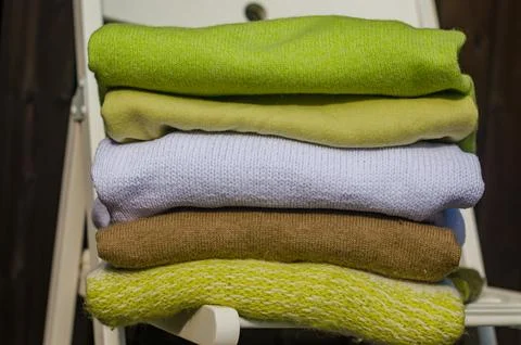 Stack of green and beige sweaters on white chair Stock Photos