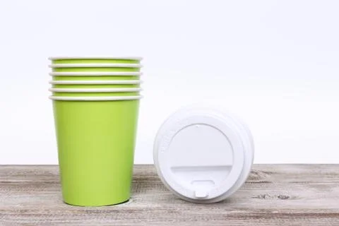 A stack of green take away disposable paper cups and plastic caps on wooden d Stock Photos