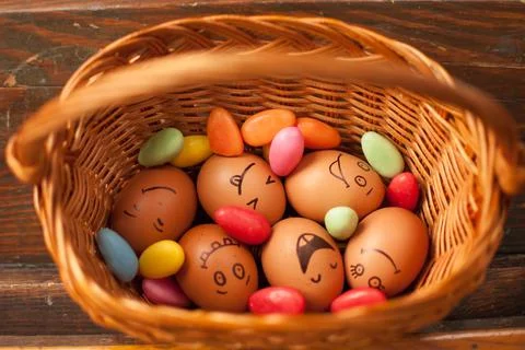 Stack of hand drawn smiley eggs on straw basket with colorful candy, easter Stock Photos
