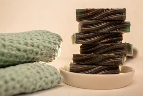 A stack of handmade soap bars rests on a white plate, with a soft green towel Stock Photos