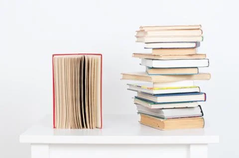 Stack of hardback books and old open book on white wall background. Search for Stock Photos