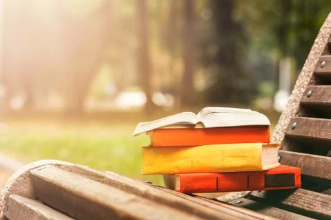 Stack of hardback books and Open book lying on bench at sunset park against Stock Photos