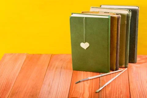Stack of hardback books, diary on wooden deck table and yellow background. Back Фото