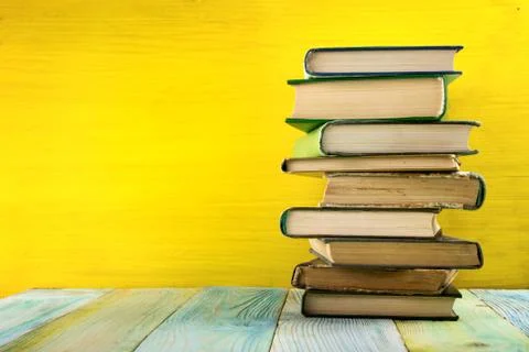 Stack of hardback books, diary on wooden deck table and yellow background. Back Stock Photos