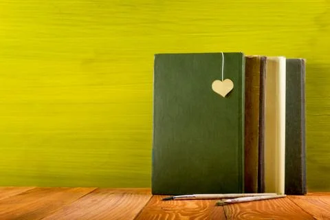Stack of hardback books, diary on wooden deck table and green background. Back Stock Photos
