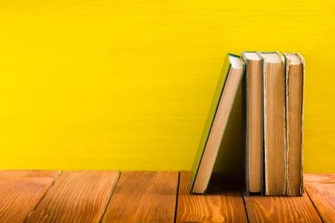 Stack of hardback books, diary on wooden deck table and yellow background. Back Stock Photos
