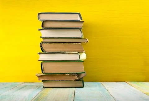 Stack of hardback books, diary on wooden deck table and yellow background. Back Stock-Fotos