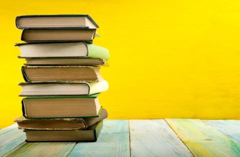 Stack of hardback books, diary on wooden deck table and yellow background. Back Stock-Fotos