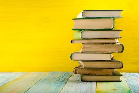 Stack of hardback books, diary on wooden deck table and yellow background. Back Stock-Fotos