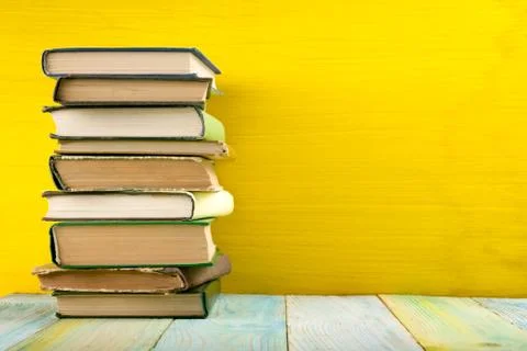 Stack of hardback books, diary on wooden deck table and yellow background. Back Foto stock