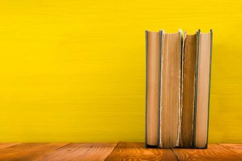 Stack of hardback books, diary on wooden deck table and yellow background. Back Stock-Fotos