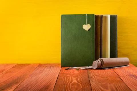 Stack of hardback books, diary on wooden deck table and yellow background. Back Stock Photos