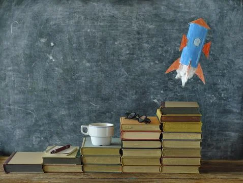 Stack of hardback books with rocket launching on blackboard background Stock Photos