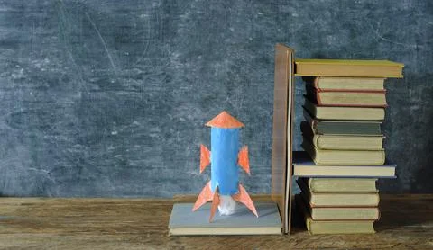 Stack of hardback books with rocketship launching on blackboard background Stock Photos