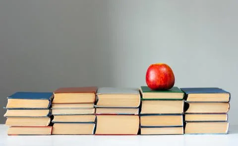 Stack of hardback books on white table with red apple. Books stacking. Back t Stock Photos